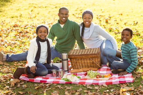 Mother, Father and Two Children Enjoy an Autumn Picnic While Sitting on a Table Cloth